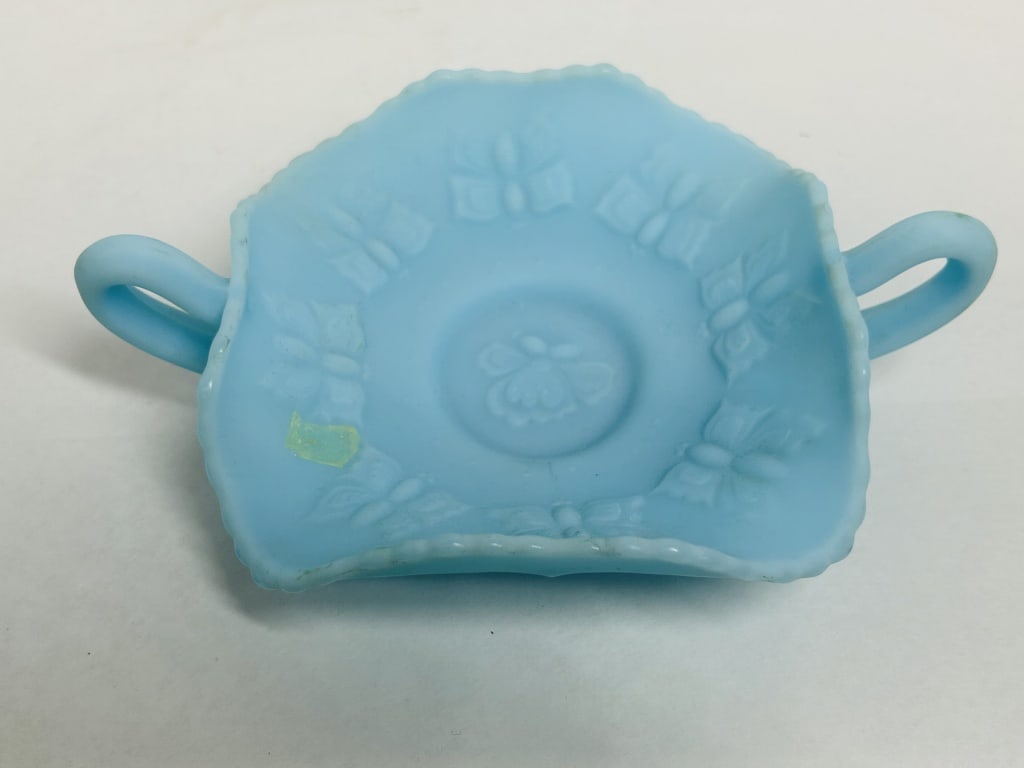 BLUE SATIN BUTTERFLY DISH, 20TH CENTURY: A light blue satin glass bonbon dish attributed to Fenton Art Glass, featuring an embossed butterfly and floral motif. The vessel is designed with a square-form ruffled rim and dual loop handles above