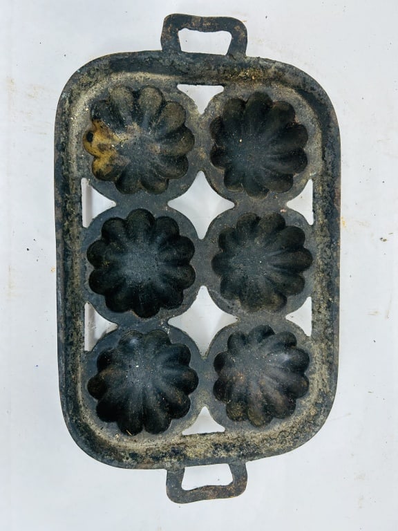 CAST IRON TURKS HEAD GEM PAN, CIRCA 1900: An antique cast iron gem pan featuring six fluted, scalloped cups in a turks head motif arranged within an open rectangular frame. The piece is designed with two integral loop handles and lacks visibl