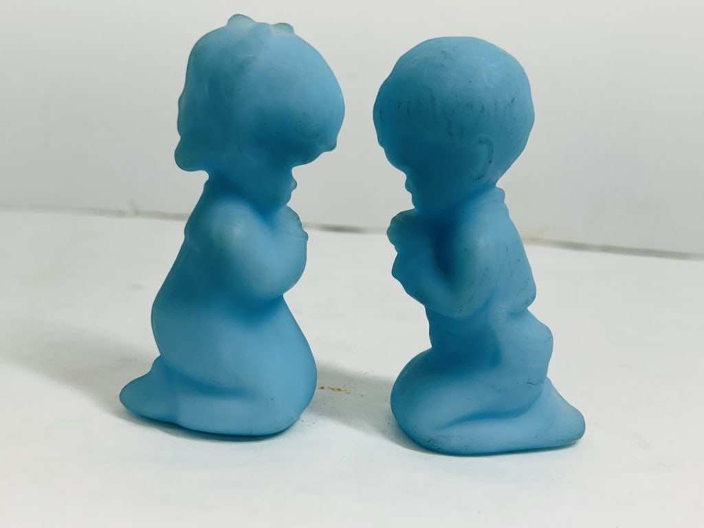 FENTON BLUE SATIN PRAYING CHILDREN, 1970S: A pair of kneeling boy and girl figurines attributed to the Fenton Art Glass Company, produced in blue satin glass. The items feature a matte finish and visible mold seams.