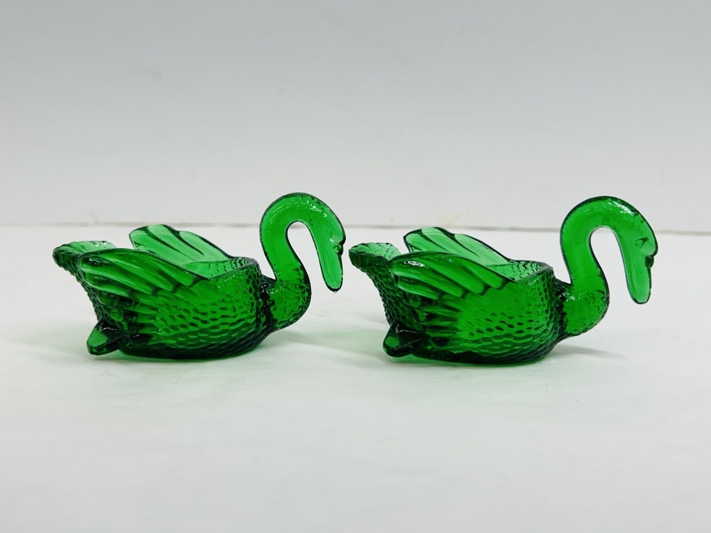 MOSSER EMERALD GLASS SWAN PAIR: A pair of emerald green pressed glass swan dishes featuring stylized wing details and a pebbled texture. The base of each piece is molded with the Mosser Glass Company shield mark.