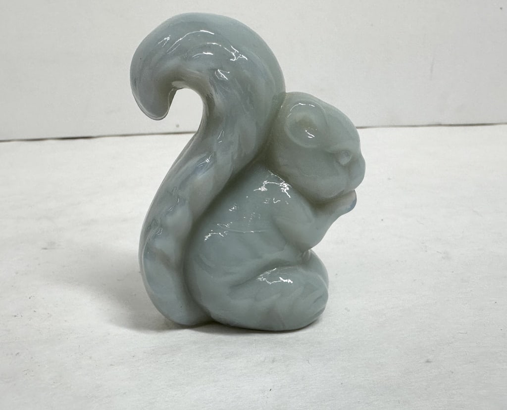 BOYD BLUE/WHITE GLASS SQUIRREL FIGURINE: A pressed slag glass figurine depicting a seated squirrel holding a nut, characterized by a swirled light blue and white color palette. The piece exhibits a vertical mold seam and a ground, slightly c