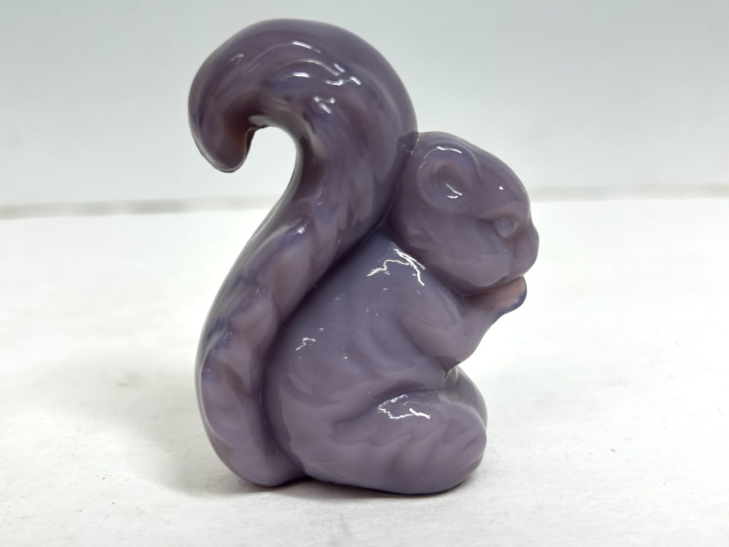 BOYD PURPLE SLAG GLASS SQUIRREL FIGURINE: A seated squirrel figurine fashioned from swirled purple and white slag glass, exhibiting mold seams consistent with press-molded production. A paper label affixed to the underside identifies the colo