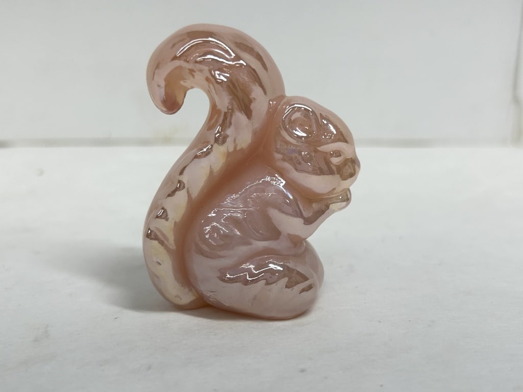 PINK IRIDESCENT BOYD SQUIRREL: A molded glass figurine of a seated squirrel holding a nut, crafted in pink opalescent glass with an iridescent finish.