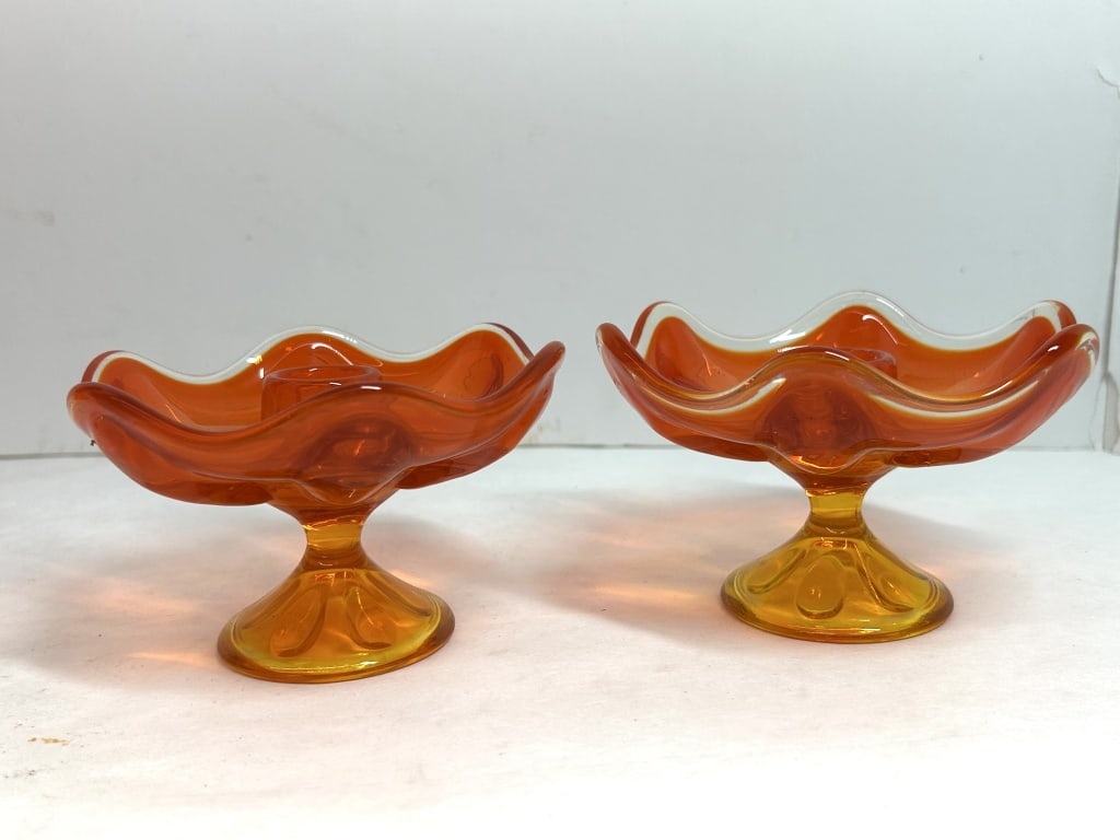 VIKING STYLE AMBERINA GLASS CANDLESTICKS, 1960: A pair of mid-century modern footed amberina art glass candle holders with ruffled rims, attributed to Viking Glass. The vibrant persimmon orange bowls transition to amber-toned pedestals on circular