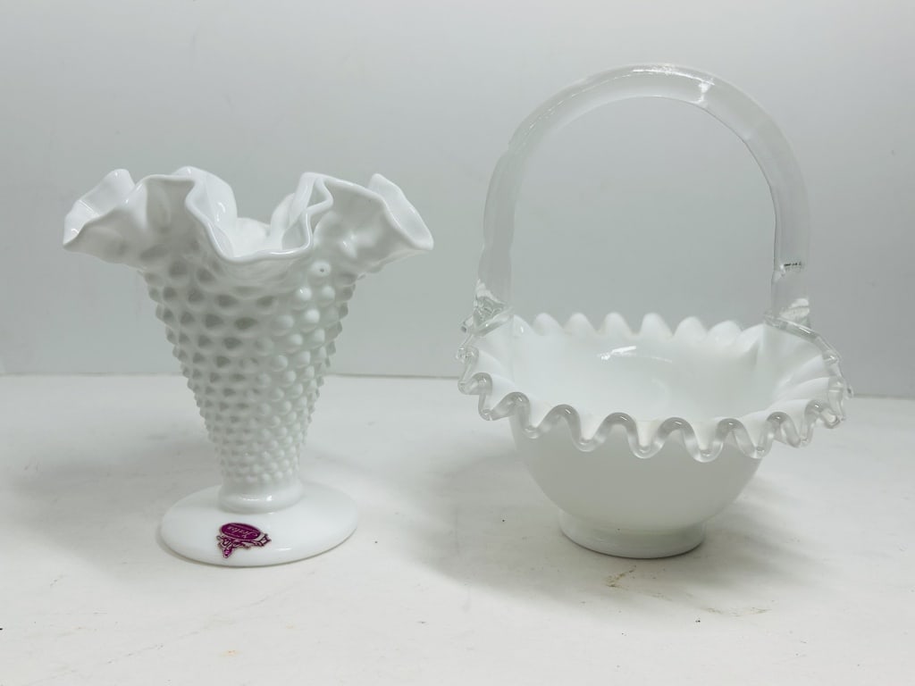 FENTON MILK GLASS ITEMS CIRCA 1970: A footed vase featuring an all-over hobnail pattern and a ruffled silver crest basket with an arched crystal handle. Both pieces bear authentic manufacturer markings including a pink foil label and an