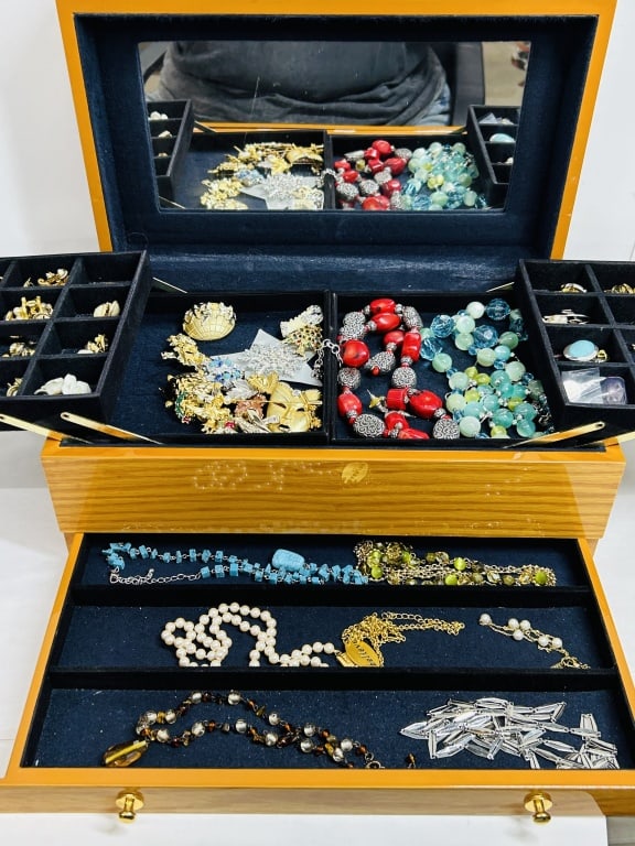 GYJOYERO BOX AND COSTUME JEWELRY, 21ST CENTURY: An assortment of costume jewelry featuring base metals, resin, and glass housed in a GYJOYERO three-tier polished wood jewelry case. The collection includes necklaces, brooches, and earrings, with not