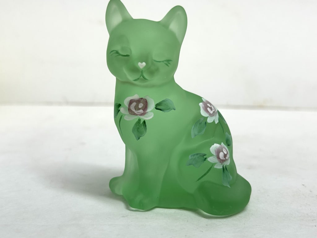 FENTON WILLOW GREEN SATIN CAT: A seated cat figurine produced by the Fenton Art Glass Company in willow green satin glass. The figure features hand-painted floral motifs and retains the original silver foil manufacturer label on th