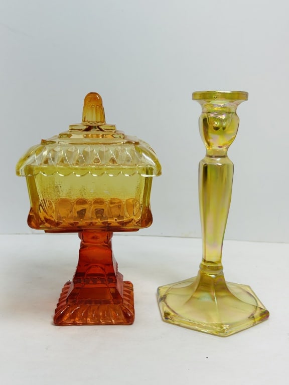JEANNETTE STYLE AMBERINA AND CARNIVAL GLASS, 1960s: This lot includes a lidded pedestal candy dish in the Wedding Box pattern attributed to Jeannette Glass Company and a faceted marigold carnival glass candlestick. Both examples represent mid-20th-cent