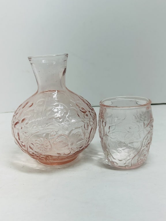 PINK DEPRESSION GLASS WATER SET, 1930S: A two-piece bedside water set featuring an embossed floral and vine motif in translucent pink glass. The design is attributed to the Hocking Glass Company's Mayfair pattern.Carafe: 6.75 inches in heig