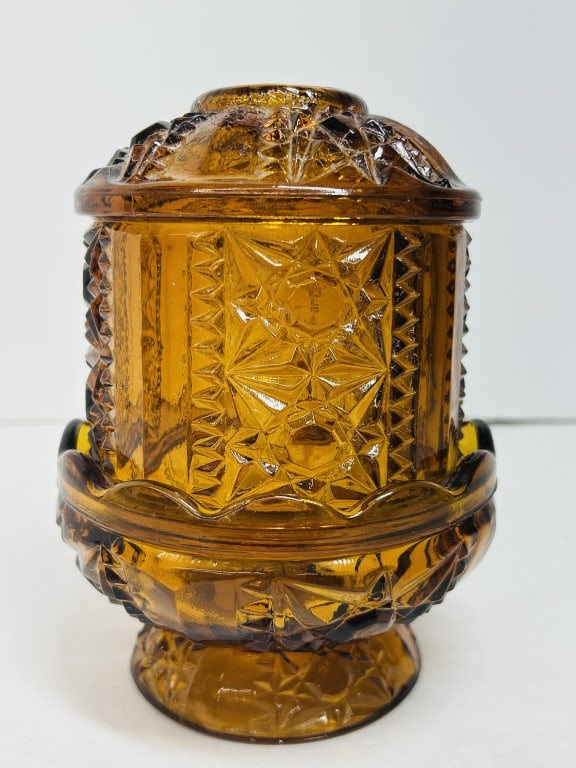 INDIANA AMBER FAIRY LAMP MID-CENTURY: A two-piece amber pressed glass fairy lamp in the Stars and Bars pattern, attributed to the Indiana Glass Company. The vessel comprises a matching footed base and domed lid adorned with geometric star