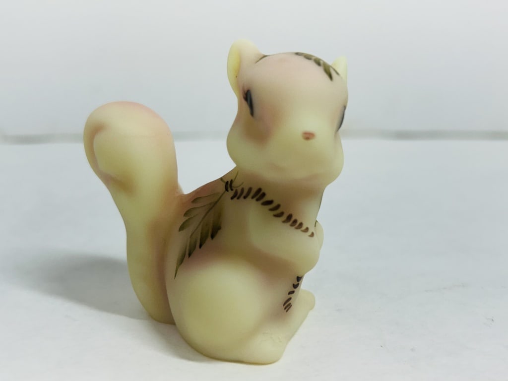 FENTON BURMESE GLASS SQUIRREL, 1970S: Hand-painted Burmese glass figurine produced by Fenton Art Glass Company featuring an autumn acorn and leaf motif. The underside is signed by factory decorator Martha Caplinger and includes the script