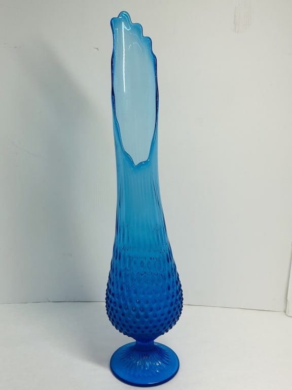 MID-CENTURY HOBNAIL SWUNG GLASS VASE: Colonial blue swung glass vase in the hobnail pattern, attributed to the Fenton Art Glass Company. The vessel features an elongated fluted neck and a pressed rayed pedestal base.Dimensions not provide