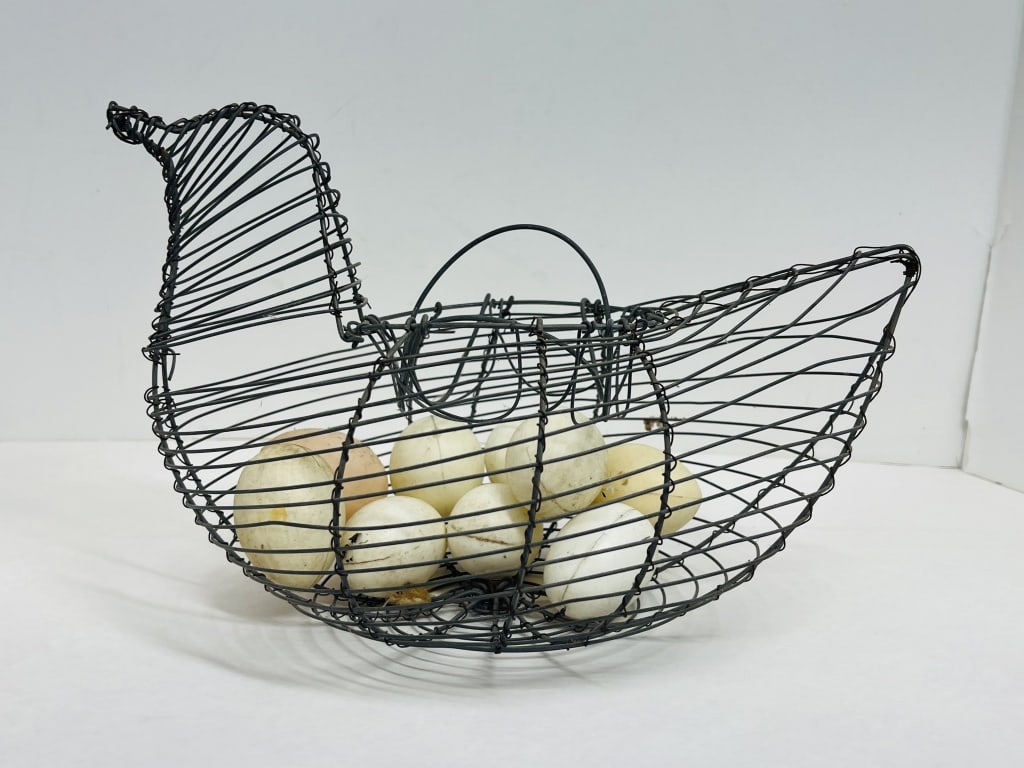 PAINTED WIRE HEN BASKET, CIRCA 1950: This mid-20th century wrought metal wire basket is fashioned in the form of a hen and contains a collection of several faux eggs. The frame features horizontal concentric ribs with two wire bail handl