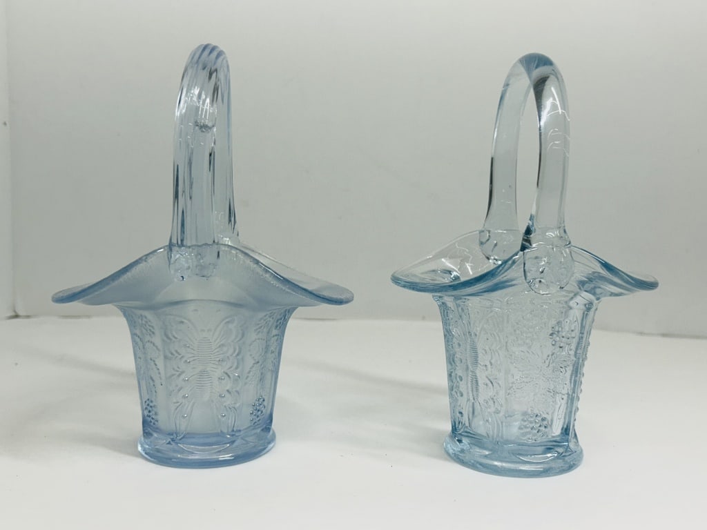 PAIR OF ATTRIBUTED FENTON GLASS BASKETS: A pair of light blue pressed glass baskets featuring the Butterfly and Berry pattern, attributed to Fenton Art Glass. The lot comprises one iridescent ice blue carnival glass example with a ribbed han