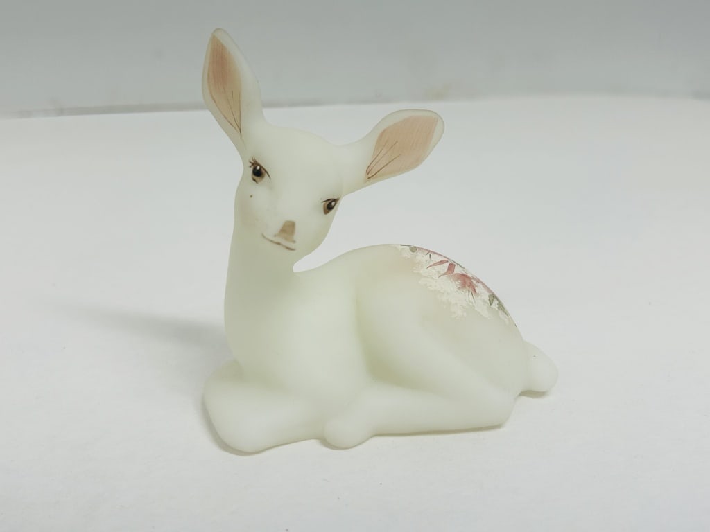 FENTON SATIN GLASS FAWN FIGURINE: A white satin glass figurine of a reclining fawn produced by Fenton Art Glass Company. The piece features hand-painted floral decoration on the flank and is signed by artist B. Cumbridge with an embos
