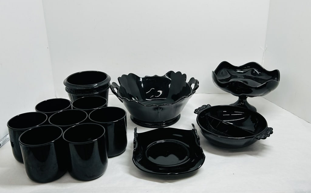 L.E. SMITH, BLACK AMETHYST GLASS, MID-20TH CENTURY: A twelve-piece collection of black amethyst glass produced by L.E. Smith. The group includes tumblers, serving bowls, a pedestal compote, and a footed cachepot with a Greek key border and silver-tone 