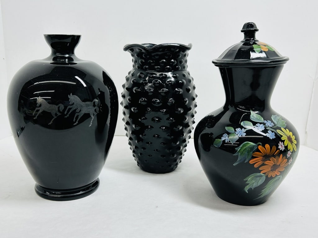 TRIO OF BLACK AMETHYST GLASS VESSELS, MID-20TH CENTURY: A trio of mid-century decorative vessels crafted from opaque black glass, featuring an acid-etched equestrian motif, a molded hobnail pattern with ruffled rim, and a hand-painted floral lidded jar. Th