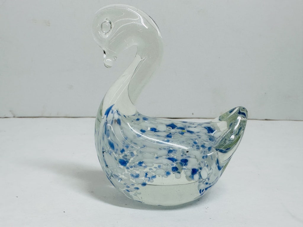 HAND-BLOWN GLASS SWAN FIGURINE, 20TH CENTURY: Hand-blown art glass swan figurine featuring a clear neck and body with encased blue and white splatter decoration. The piece contains small internal air bubbles consistent with artisanal production.