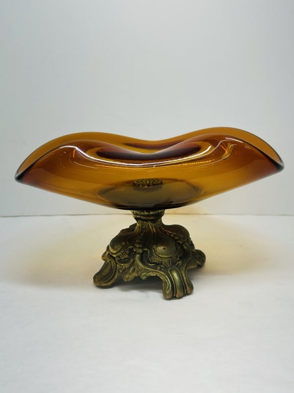 MURANO AMBER GLASS CENTERPIECE BOWL, MID-20TH CENTURY: Murano hand-blown amber glass centerpiece bowl featuring a ruffled swung rim with a dark brown trailed edge. The vessel is mounted to a four-footed cast metal pedestal base decorated with ornate Rococ