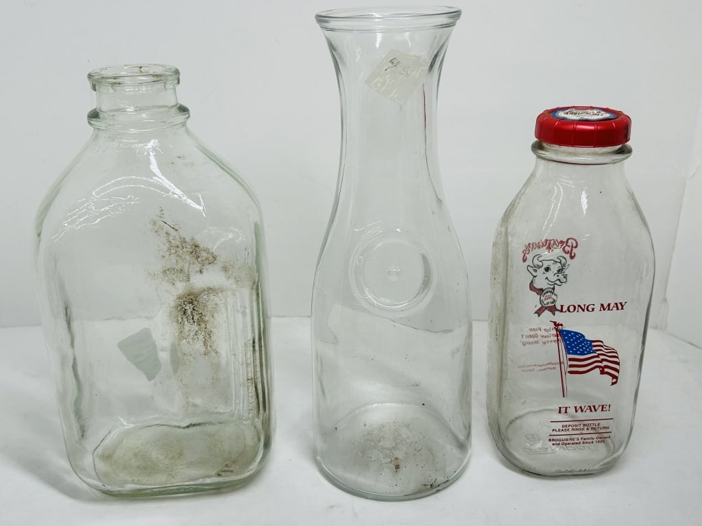 BROGUIERE'S DAIRY GLASS VESSELS, 1990S: Three molded clear glass vessels featuring a Broguiere's Dairy quart milk bottle with screen-printed patriotic graphics and a red plastic cap. The collection also includes a tall flared glass carafe a