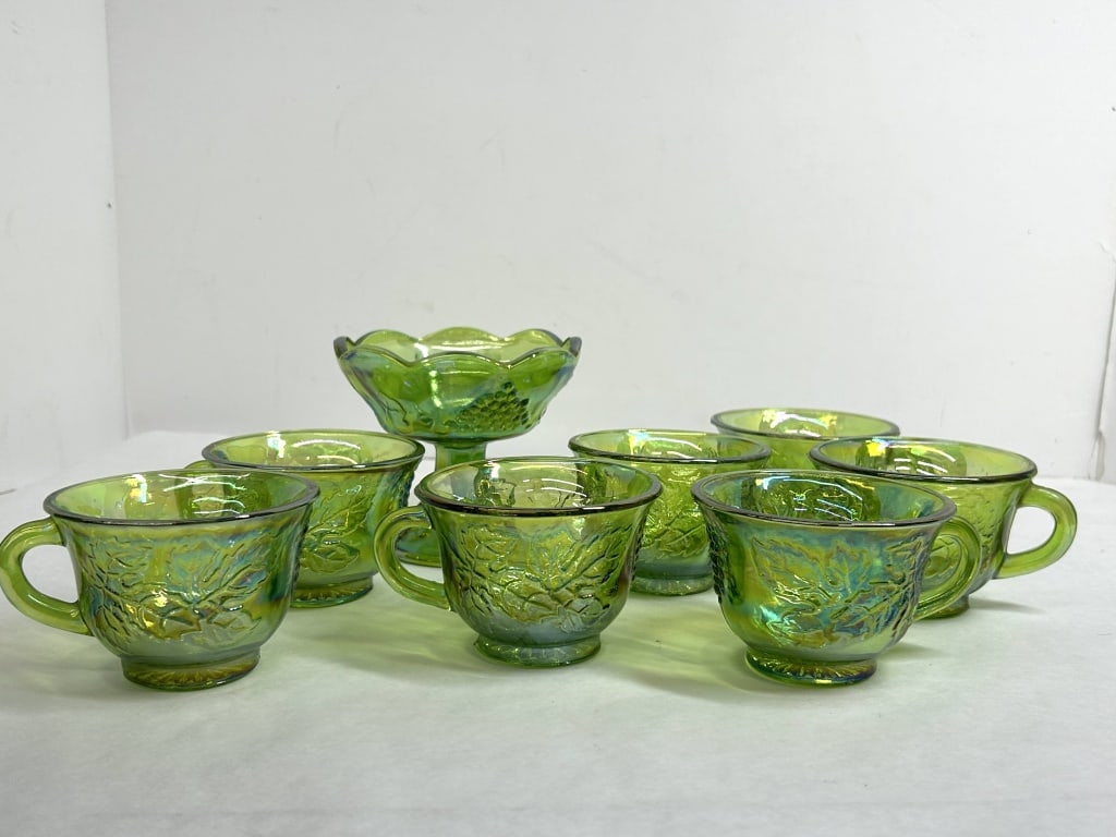 INDIANA GLASS HARVEST GRAPE SET 1970S: A set of eight pieces of green iridescent pressed glass manufactured by the Indiana Glass Company in the Harvest Grape pattern. The group includes seven punch cups and a coordinating pedestal base fea