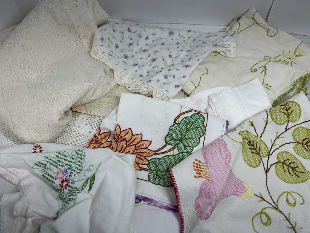 VINTAGE EMBROIDERED COTTON LINENS, CIRCA 1950: An assortment of household linens featuring hand-embroidered floral motifs and rosebud prints. Materials include cotton and linen fabrics decorated with fill-stitch needlework and various lace trims.