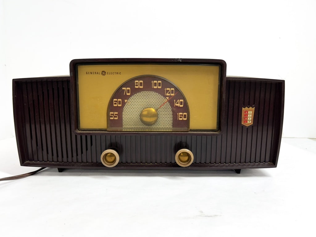 GENERAL ELECTRIC BAKELITE RADIO, 1955: Vacuum tube AM radio produced by General Electric featuring a brown Bakelite cabinet and Dial Beam tuning display. The unit includes original control knobs and a rear auxiliary phono input.