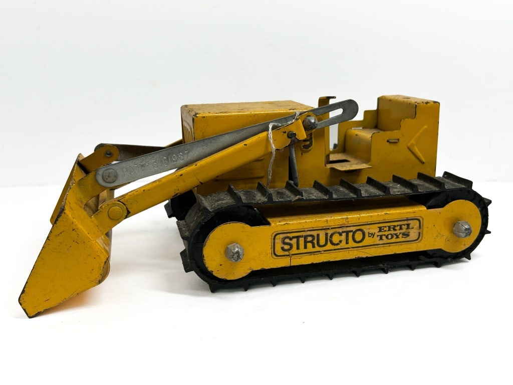 STRUCTO BY ERTL BULLDOZER LOADER 1960S: Structo by Ertl pressed steel bulldozer loader featuring a manual lever-operated lift mechanism and flexible black tracks. Side decals identify the manufacturer, and the loader arm is embossed with