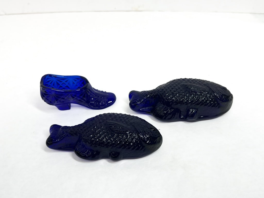 BOYD COBALT GLASS SLIPPER AND FISH, 1983-1988: A trio of cobalt blue pressed glass decorative items comprising a slipper and two figural fish. The slipper is produced by Boyd's Crystal Art Glass and features a Daisy and Button pattern with a mark