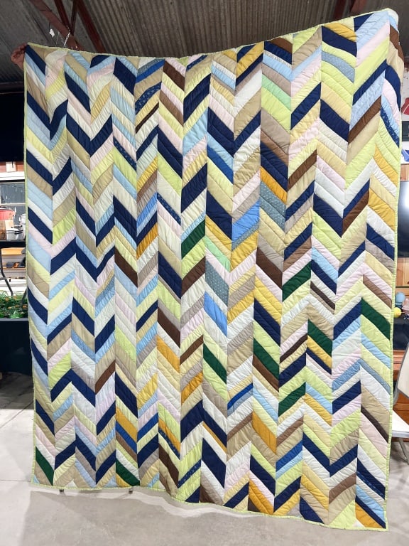 Handmade Multi-Color Pieced Chevron Scrap Quilt: This large handmade quilt features a multi-color chevron or zigzag pattern across the entirety of the top. The top is constructed from numerous machine-pieced fabric strips in a variety of solid and