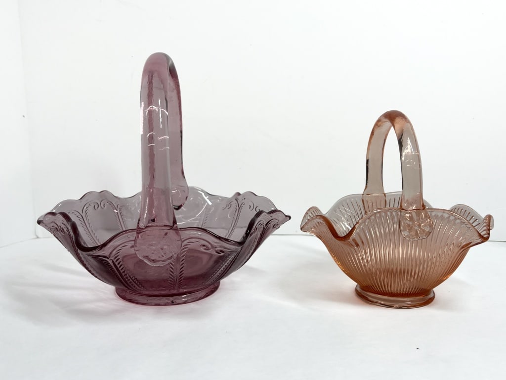 FENTON GLASS BASKETS, 20TH CENTURY: Two Fenton Art Glass baskets, including an amethyst example in the Inverted Strawberry pattern and a pink example with optic ribbing. Both pieces feature ruffled rims and hand-applied handles.