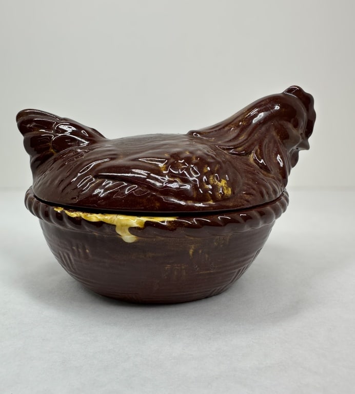 HULL POTTERY CERAMIC HEN ON NEST: Mid-century lidded earthenware hen on nest produced by Hull Pottery. The piece features a high-gloss brown drip glaze over a cream-colored body, with a molded basket-weave pattern to the base and an i