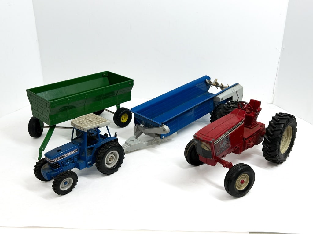 ERTL FOUR DIE-CAST TOYS, 1980S: A collection of four vintage farm toys manufactured by Ertl, featuring a Ford TW-5 tractor, an International Harvester style tractor, a manure spreader, and a gravity wagon. The pieces are constructed