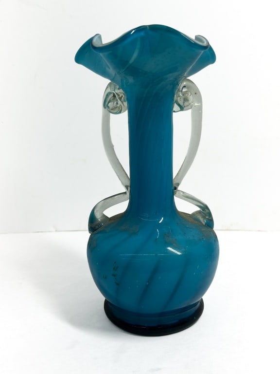 TURQUOISE ART GLASS DOUBLE HANDLED VASE: Hand-blown turquoise art glass vase featuring a twisted rib bulbous body and a ruffled rim. The vessel is finished with two applied clear glass handles and sits on a dark cobalt or black circular foot
