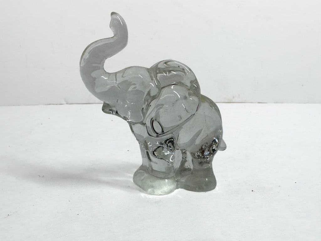 HEISEY CLEAR GLASS ELEPHANT FIGURINE: A.H. Heisey and Company molded clear glass figurine depicting an elephant with its trunk raised. The piece features the signature embossed H in a diamond trademark on the base of one foot.