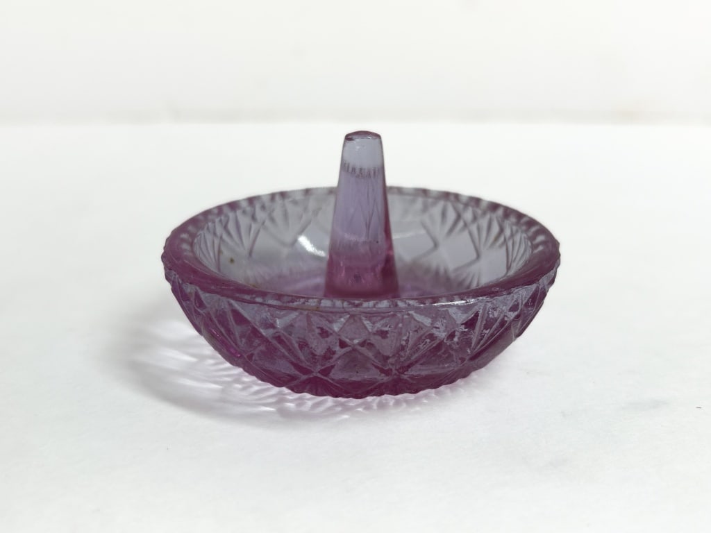 AVON AMETHYST GLASS RING HOLDER VINTAGE: Avon amethyst glass ring holder. The bowl features a diamond-point exterior and a central sunburst pattern with an embossed oval maker mark on the underside of the post.
