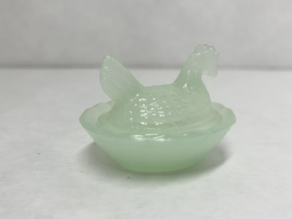 JADEITE STYLE SATIN GLASS HEN ON NEST: Miniature two-piece lidded dish in the form of a hen on a nest, crafted from pale green jadeite-style glass with a satin finish. The piece features a molded hen cover with detailed feathering and an