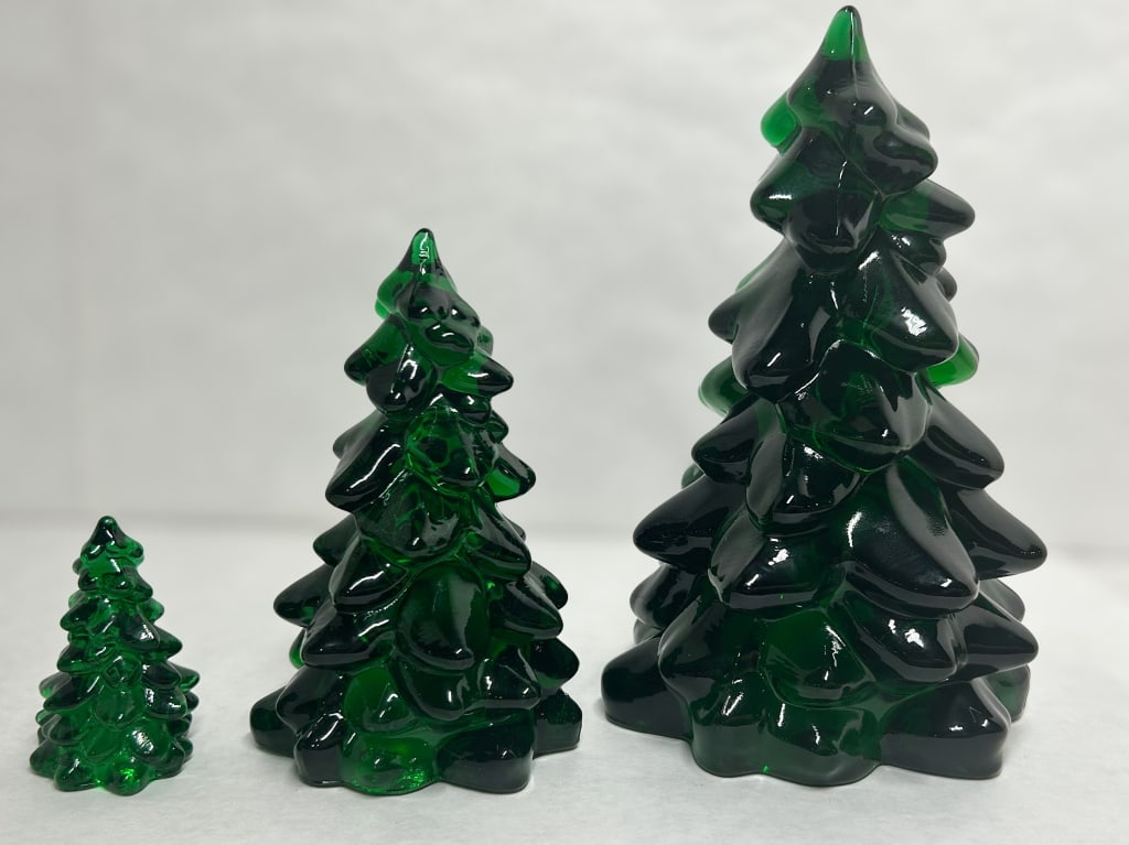 MOSSER EMERALD GREEN GLASS TREES: A trio of emerald green glass Christmas trees produced by Mosser Glass. The figurines feature stylized tiers of rounded boughs in translucent glass with polished bases. Large: 8 inches Medium: 6 inche