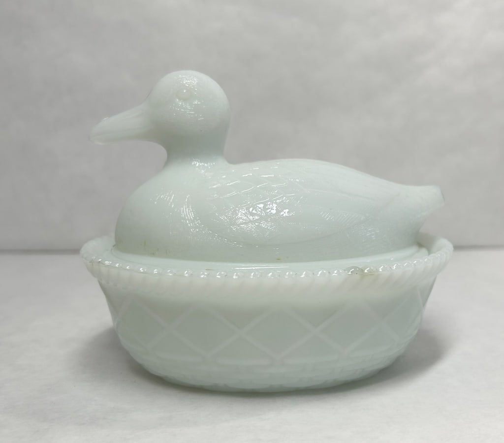 AMERICAN MILK GLASS DUCK, 20TH CENTURY: An American milk glass covered dish in the form of a duck on a nest. The base features a basketweave pattern with a cabled rim and an embossed mold number 6 on the interior bottom.