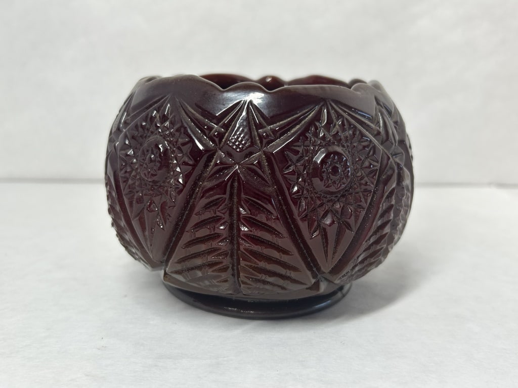 FENTON PIGEON BLOOD GLASS ROSE BOWL: Fenton pressed glass rose bowl featuring a deeply pressed geometric pattern of stars and pinwheels with a scalloped rim. A rectangular handwritten paper label in the interior reads "Fenton Rose bowl (