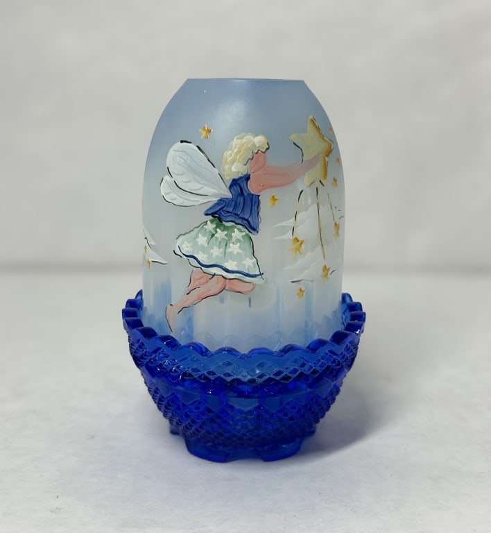 FENTON COBALT SATIN GLASS FAIRY LAMP: A two-piece fairy lamp produced by Fenton Art Glass Company, featuring a cobalt blue pressed glass base and a hand-painted blue satin glass shade. The shade is decorated with a blonde fairy reaching t