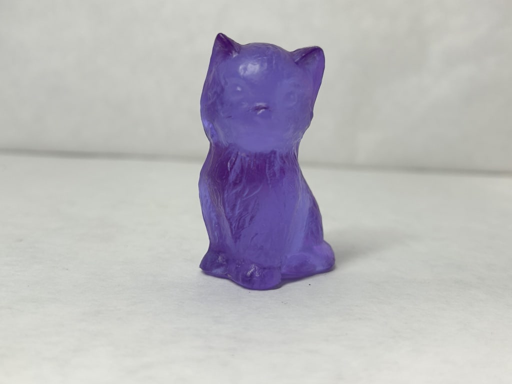 BOYD MISS COTTON PURPLE GLASS KITTEN, 1980S: Miniature seated kitten figurine produced by Boyd's Crystal Art Glass in translucent amethyst glass. A molded B in a diamond mark with a horizontal line above is visible on the lower reverse (photo 5)