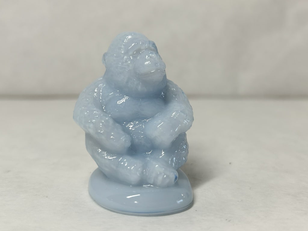BOYD SONNY THE GORILLA LIGHT BLUE: Seated gorilla figurine crafted in light blue opalescent slag glass. An impressed monogram consisting of a diamond border containing a character, flanked by a vertical line, is visible on the lower re