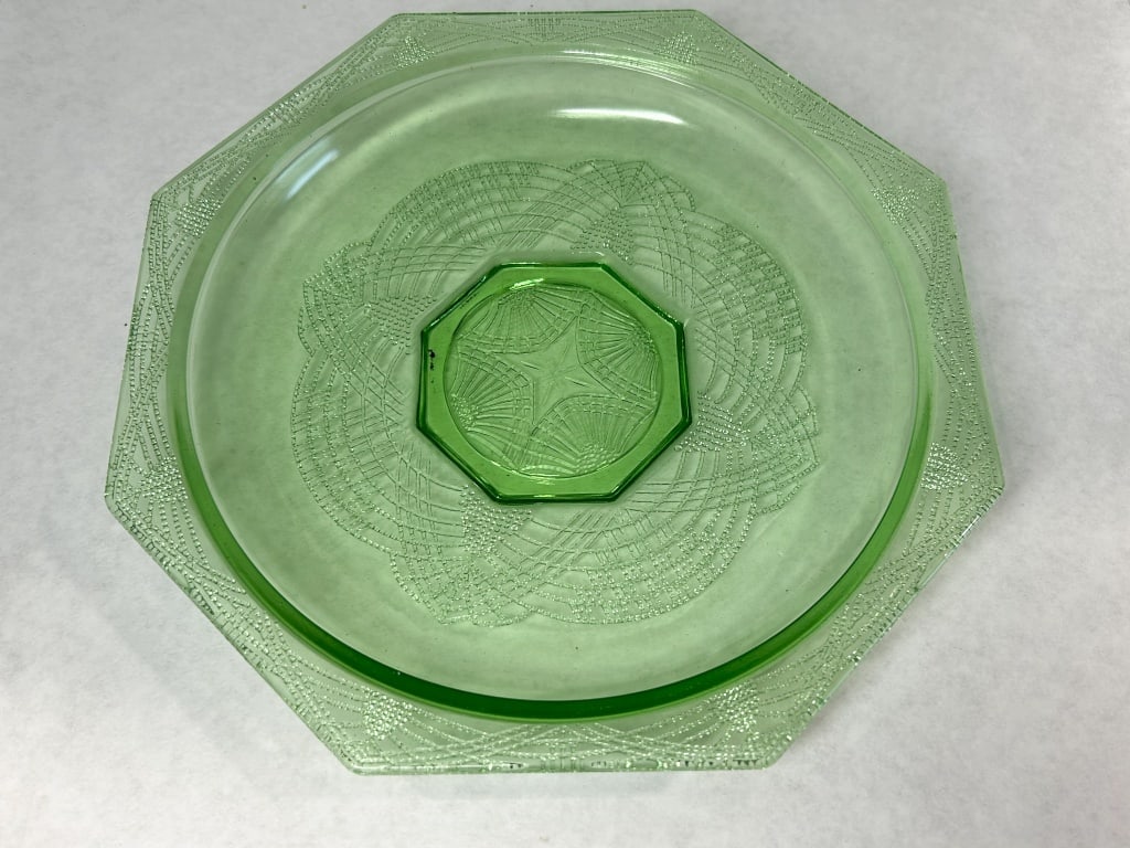 ROMANESQUE PATTERN URANIUM GLASS PLATE, 1930S: A green pressed glass plate featuring an octagonal form with a central star medallion and interlocking swag border. The uranium-infused glass displays bright neon green fluorescence under ultraviolet 