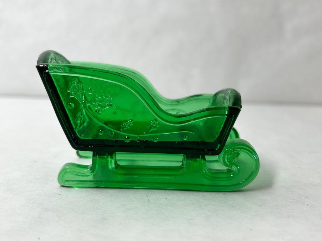 MOSSER GREEN GLASS HOLIDAY SLEIGH: Pressed glass holiday sleigh produced in a transparent forest green color. The exterior features a molded relief pattern of holly leaves and berries with scrolled runners and a stippled texture on