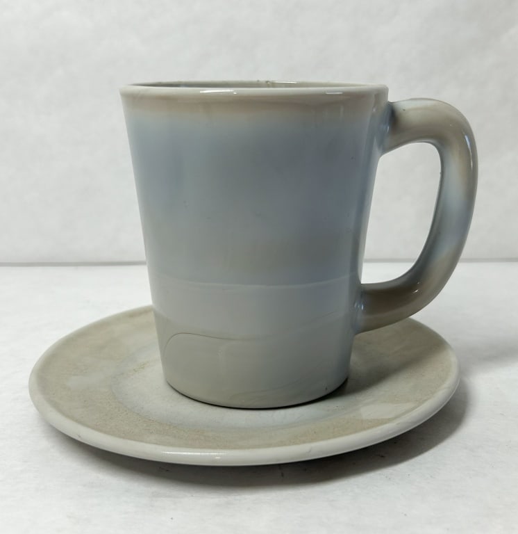 MOSSER MARBLE MUG AND SAUCER: A vintage stoneware mug and saucer set featuring a scroddled clay body with marbled swirls of blue, gray, and tan under a clear glaze. An embossed capital letter M within a square border is present