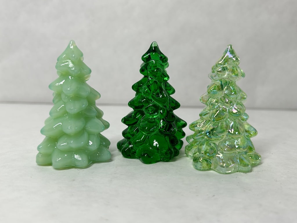 MOSSER GREEN TRIO OF GLASS CHRISTMAS TREES: Three miniature pressed glass Christmas tree figurines in jadeite, emerald green, and iridescent finishes. No maker marks or labels are visible on the exterior surfaces.