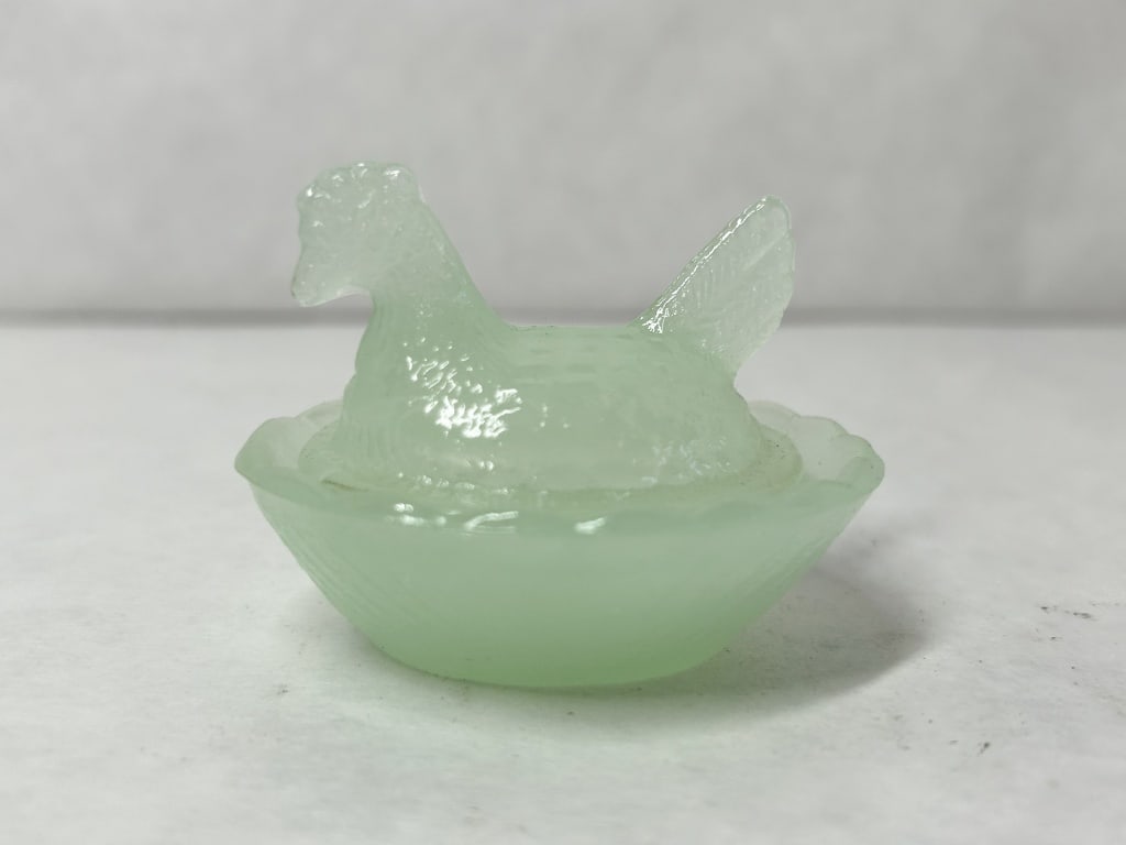 MINIATURE JADEITE GLASS HEN ON NEST: A two-piece miniature pressed glass covered dish in the form of a hen on a nest. The set is composed of semi-translucent mint green glass featuring a molded lid with textured plumage and an oval