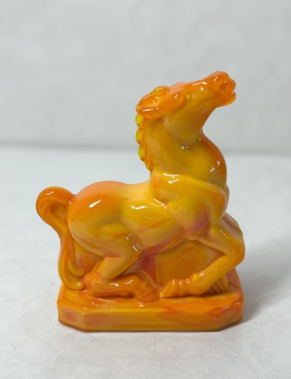 DEGENHART ORANGE SLAG GLASS HORSE FIGURINE, CIRCA 1975: Pressed slag glass figurine of a reclining horse in Persimmon slag glass produced by Crystal Art Glass (Degenhart). An embossed diamond mark containing a capital letter D is visible on the center fron
