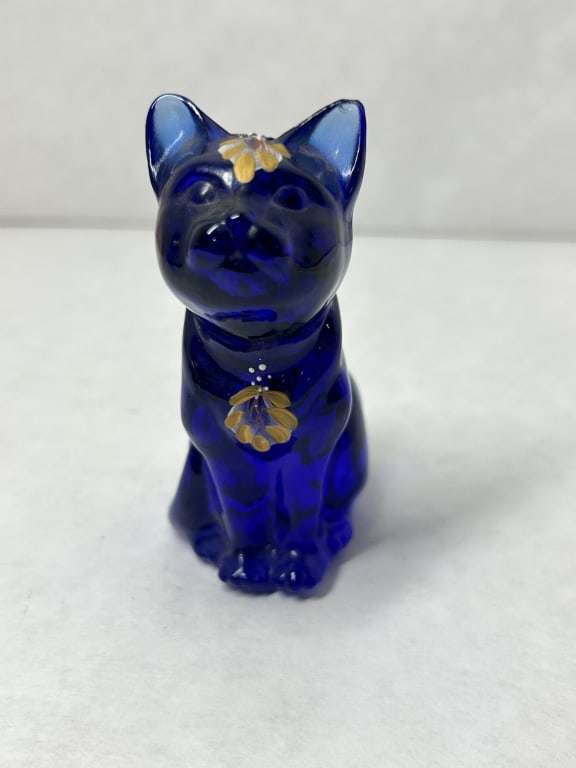 FENTON COBALT GLASS CAT, 1970s: A Fenton Art Glass hand-painted cobalt blue figurine of a seated cat decorated with gold and white floral motifs. The piece is signed in white script by artist V. Watson and bears an embossed script f